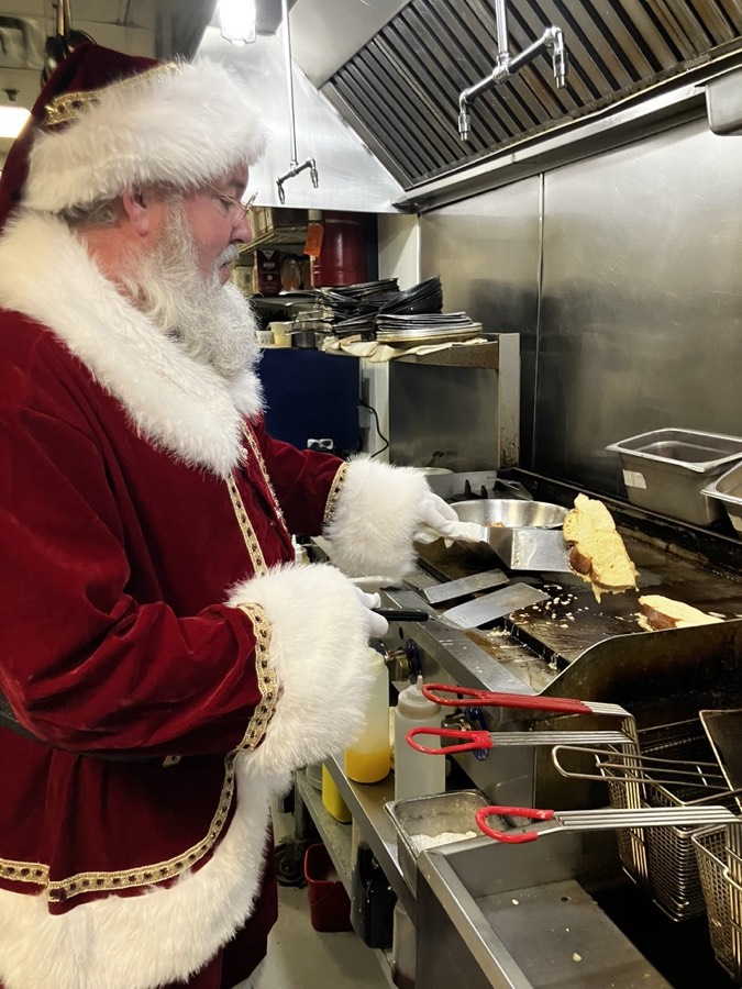Santa flipping French toast on a restaurant griddle